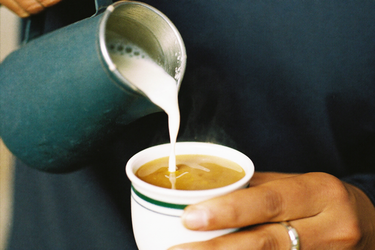 Steamed milk being poured into a white cup, a pattern forming