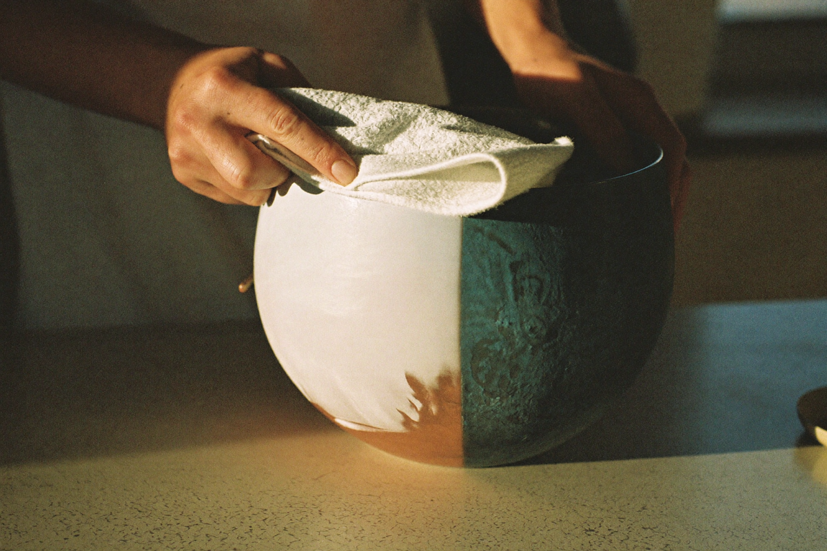 Hands polishing a copper vessel with a cloth, half bright and half dull