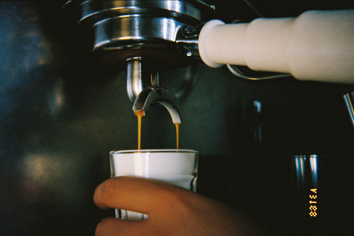 Espresso falling from a bare metal basket in two converging ropes into a small glass held steady below.