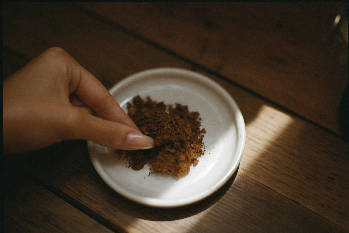 A small white dish of coarse ground coffee, fingers pinching a little of it to feel the texture.