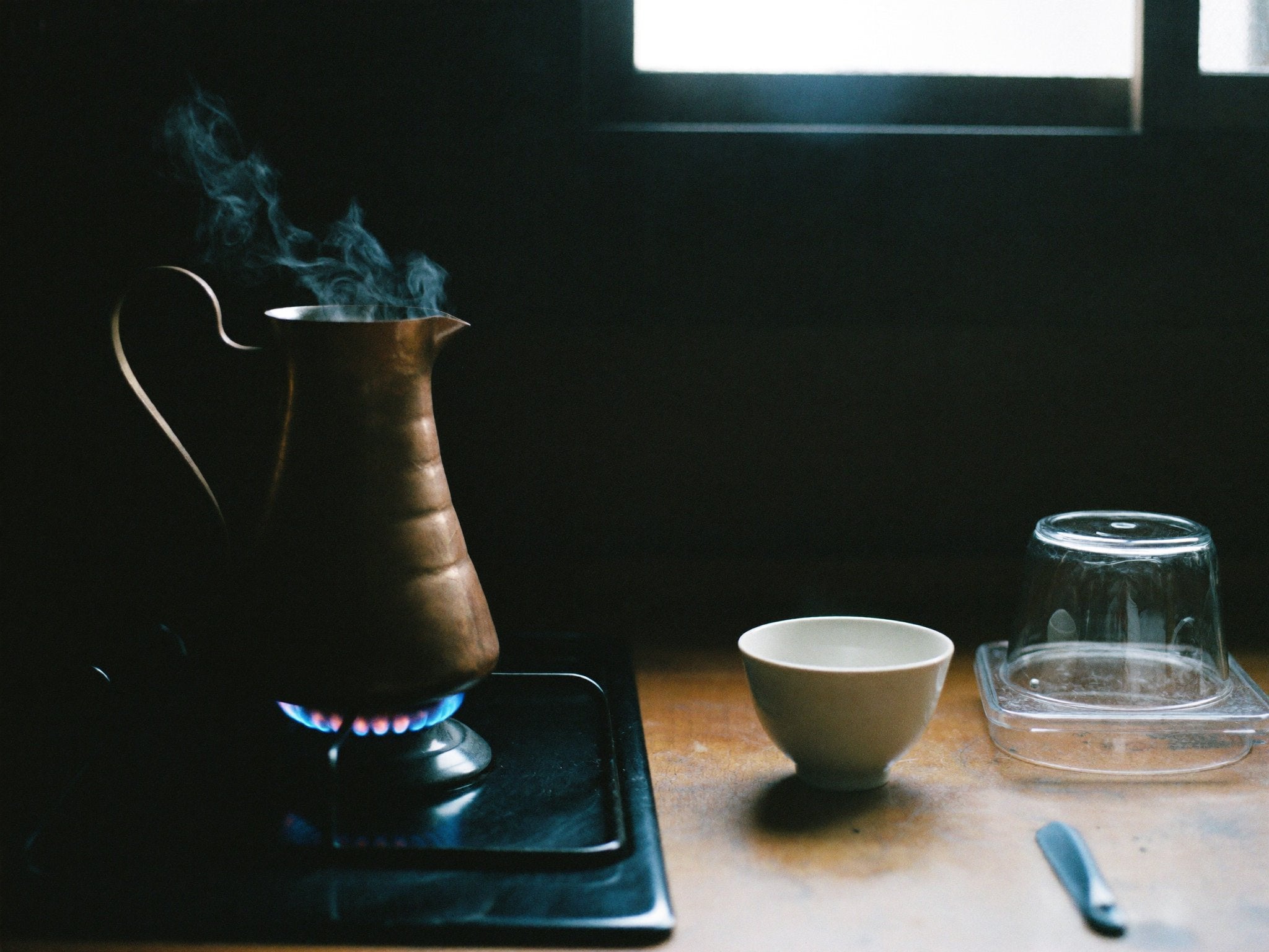 A copper pot on a low gas flame, a ceramic cup and a glass waiting on the counter beside it