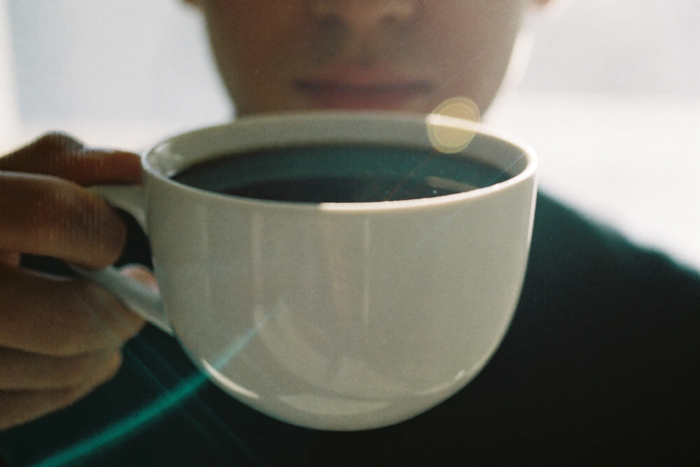 A white cup of black coffee held against a bright window