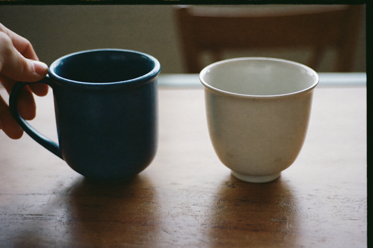 A heavy stoneware mug beside a thin porcelain cup on a wooden table