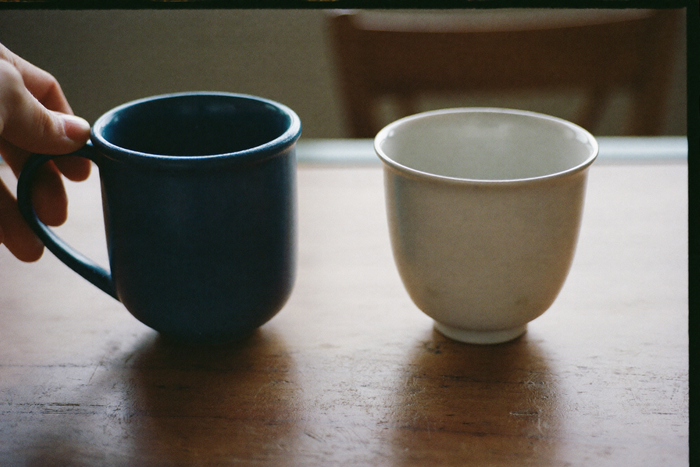 A heavy stoneware mug beside a thin porcelain cup on a wooden table