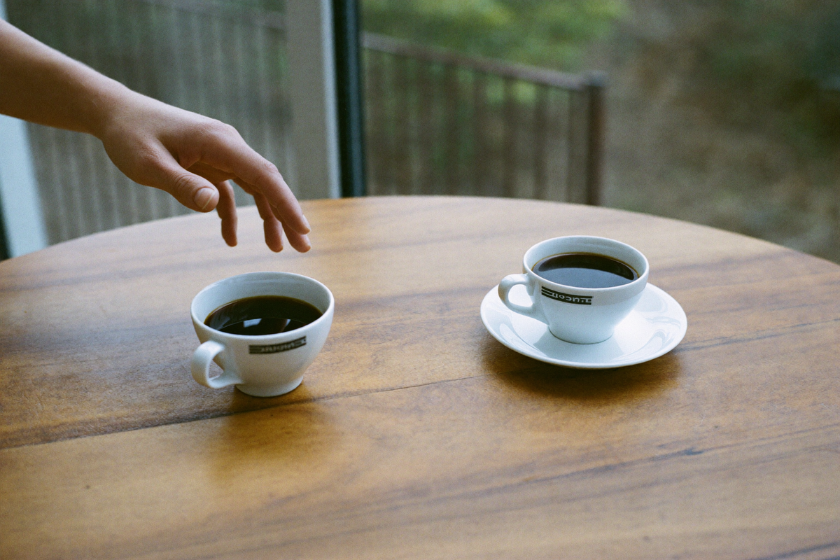 Two identical cups of coffee with a hand hovering undecided between them