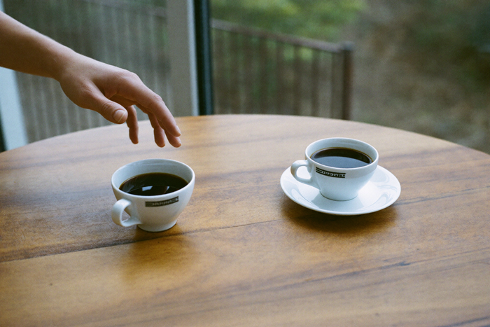 Two identical cups of coffee with a hand hovering undecided between them