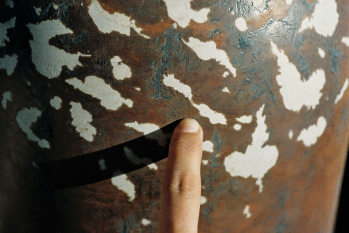 A fingertip resting on the mottled patina of an old copper surface