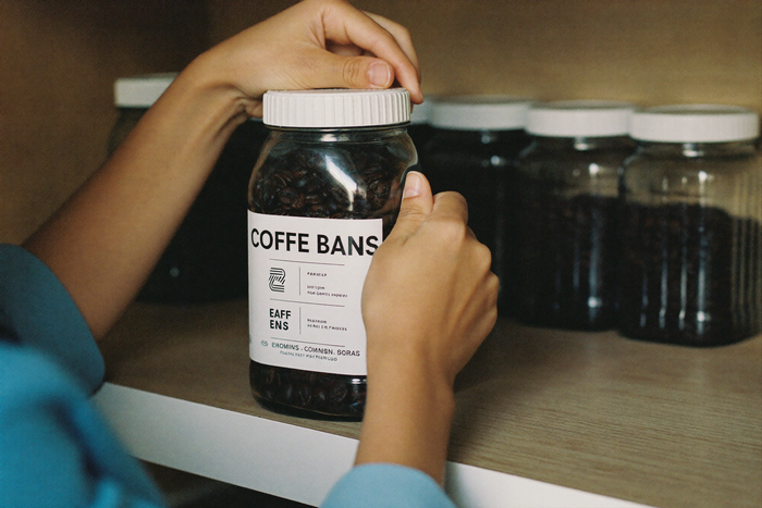 Hands closing a plain glass jar of roasted coffee beans