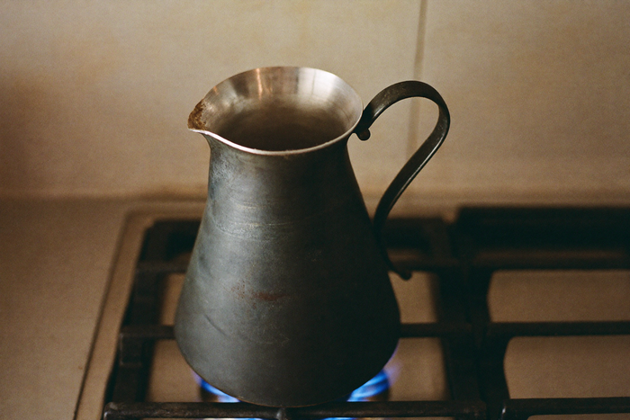 A copper cezve on a stovetop with its tin lining visible in the neck