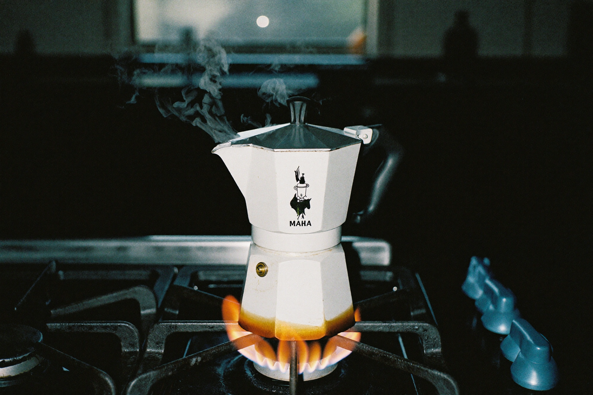A moka pot on a gas hob, coffee bubbling up at the spout