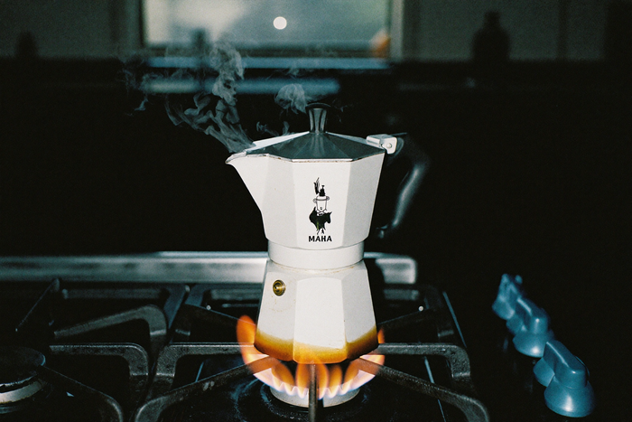 A moka pot on a gas hob, coffee bubbling up at the spout