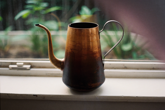 A tarnished copper cezve on a windowsill in grey afternoon light