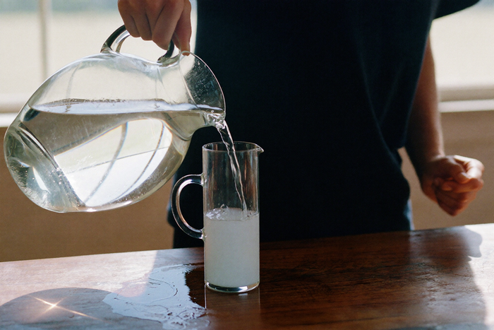 Water poured from a glass jug into a tall carafe
