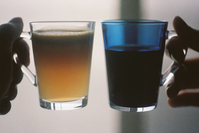 Two glass cups of coffee held against a window, one pale and one dark