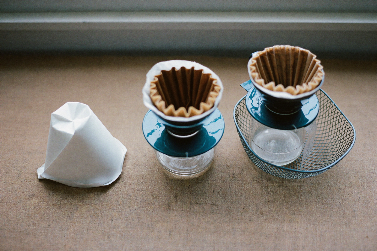 A paper cone, a cloth filter and a metal mesh basket laid on linen