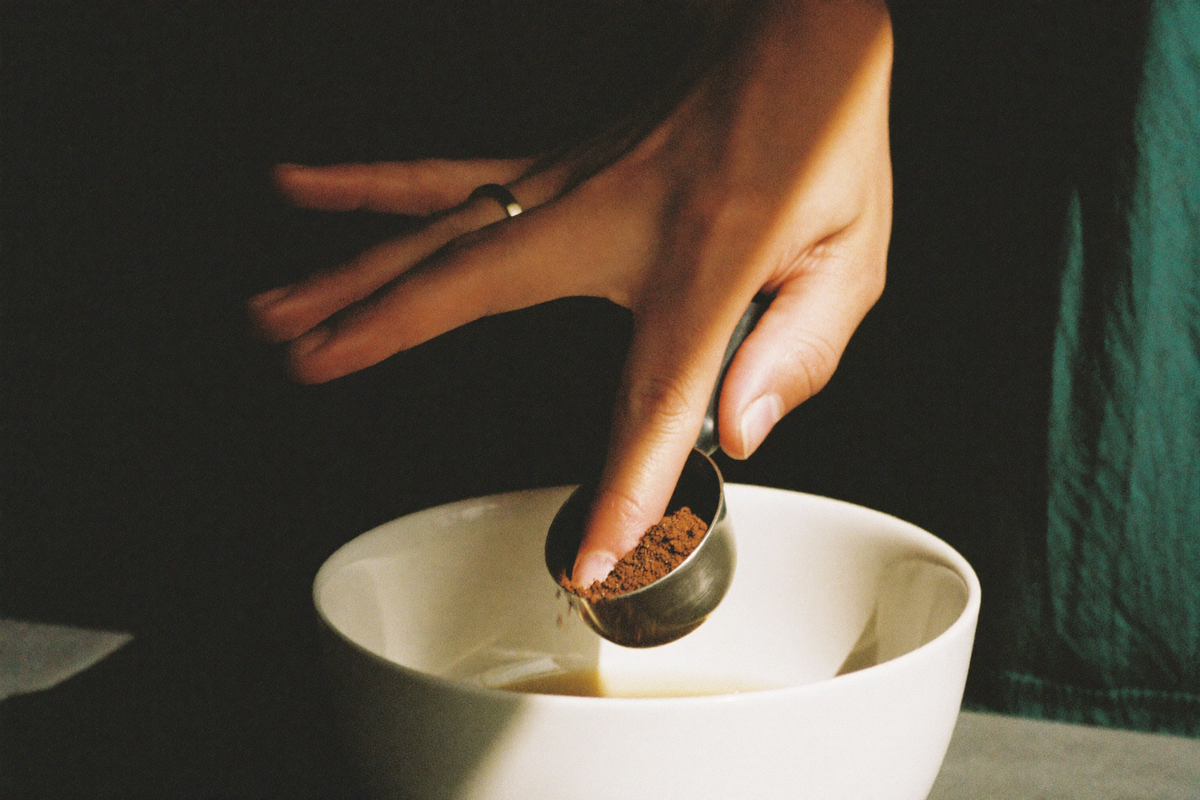 A hand levelling a heaped scoop of ground coffee over a bowl