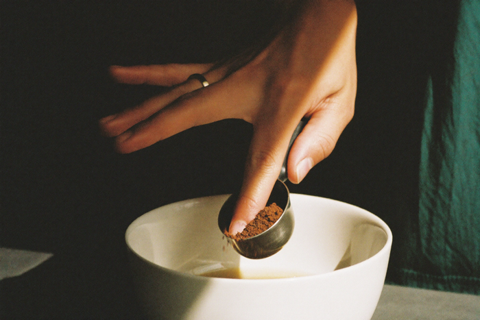 A hand levelling a heaped scoop of ground coffee over a bowl