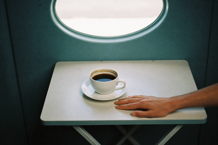A plain white cup of black coffee on a narrow fold-down table, flat daylight through a small oval window behind.