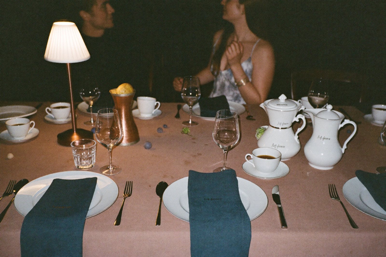 A laid table at night, porcelain coffee service and a copper vessel among the glasses
